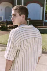 Camisa de manga corta a rayas verticales color crudo y verde, con cuello resort, corte holgado y cierre frontal con botones.