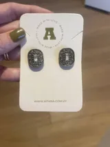 Par de aros Aitana de metal color bronce con forma cuadrada y diseño labrado. Presentan un cristal rectangular en el centro.