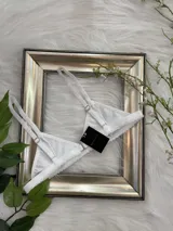 Bralette blanco de lycra con corte triangular, breteles regulables y cierre de gancho en la espalda.