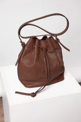 Cartera tipo botellero de cuero negro con efecto trenzado, tamaño mediano, cierre con frunce, correa ajustable con hebillas para usar al hombro o cruzada, doble bolsillo interior (uno con cierre) y forro de algodón.