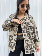 Campera de jean color beige con estampado animal print en tonos marrón y negro. Tiene cuello clásico, cierre frontal con botones, bolsillos con solapa y detalle de flecos en los bordes.