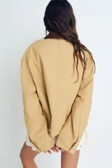 Campera color beige de algodón Oxford con cuello de pana marrón en contraste. Modelo de corte holgado con cierre frontal, hombros caídos, bolsillos laterales ribeteados y bolsillo superior con cierre. Ajuste con botones a presión en los puños y en la parte posterior del bajo.