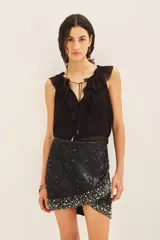 Falda corta negra de tiro medio, confeccionada en viscosa crepe, con bordado de lentejuelas y piedras en tonos plateados y blancos, concentrados principalmente en el ruedo.