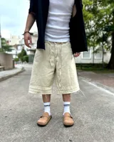 Bermuda de corte baggy color beige crema, con costura vertical trasera en cada pierna y detalle artesanal visible en el bajo. Incluye un cordón extra confeccionado en la misma tela.