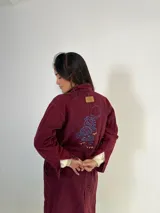 Tapado largo de jeans azul con bordado en la espalda, cuello camisero, bolsillos laterales y cierre frontal con botones.