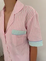 Conjunto de pijama de algodón a rayas verticales rosas y blancas, con detalles en celeste. Incluye camisa de manga corta con botones y bolsillo en el pecho, y shorts con cintura elástica.