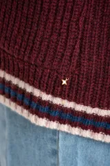 Cardigan de lana color bordó con cuello V y botones frontales. Presenta ribetes en el cuello, puños y ruedo con rayas en color beige y azul marino. Posee dos bolsillos frontales.