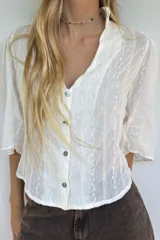 Blusa blanca de algodón liviano con bordado delicado, manga 3/4, botones frontales y volado en el cuello.