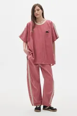 Remera oversized de denim color rosa lavado, con mangas caídas, cuello a contratono color crema y bordados en el frente.