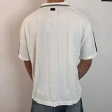 Chomba negra tejida con cuello tipo polo, mangas cortas con rayas blancas y logo estampado en el pecho.