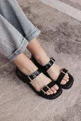 Sandalias bajas negras de cuero con base cuadrada, dos tiras anchas con hebillas plateadas y detalles de tachas pequeñas en la suela.