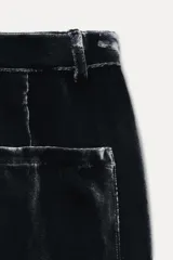 Pantalón de terciopelo negro de tiro medio, con bolsillos delanteros y traseros, pierna recta y cierre frontal con cremallera, botón y gancho metálico.