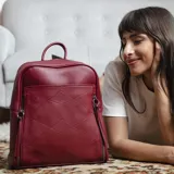 Mochila negra de símil cuero con costuras diagonales en el frente. Tiene un bolsillo frontal con broche magnético, asa de mano y correas regulables.