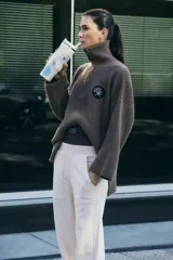Sweater marrón de punto con cuello polo, cierre de cremallera parcial y parche bordado en el pecho.