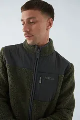Campera de sherpa verde con detalles en negro, cuello alto, cierre frontal y bolsillo con cierre en el pecho.
