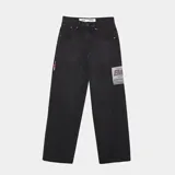 Pantalón de denim negro lavado, corte ancho (loose fit) y tiro alto, con etiqueta rectangular estampada en el muslo derecho y detalle de cinta con colores en el bolsillo delantero izquierdo.