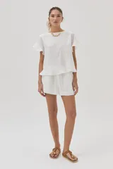 Blusa blanca de lino de manga corta, con volados en las mangas y espalda cruzada adornada con volados.