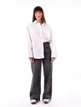 Camisa blanca con rayas verticales negras, de corte holgado, manga larga con puños abotonados y bolsillo en el pecho.