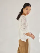 Remera gris de algodón con mangas color beige con bordados de líneas en blanco, amarillo y gris.