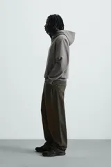 Sudadera con capucha color crudo, de corte relajado, confeccionada en tejido de algodón con interior rizado. Cuenta con cuello con capucha, manga larga, bolsillo frontal tipo canguro y acabados en rib.