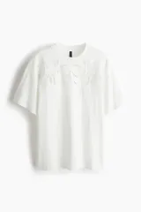 Remera blanca de algodón con cuello redondo y mangas cortas. Presenta un diseño calado en el frente.