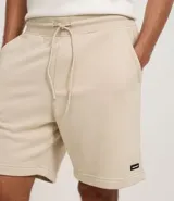 Bermuda masculina de corte slim fit, color marrón, confeccionada en algodón con felpa. Presenta cintura elástica con cordón ajustable y bolsillos laterales.