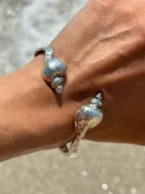 Brazalete rígido dorado con forma de caracola en los extremos.