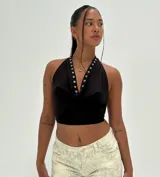 Top negro tipo halter, ajustado al cuerpo, con escote drapeado y detalles de ojales metálicos plateados a lo largo del borde del escote.