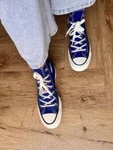 Zapatillas de lona blancas de caña alta con cordones y puntera de goma. Logo de durazno engomado en la base y en la cara interna.