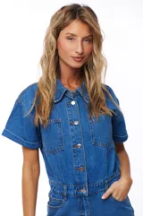 Mono corto de jean azul con cuello camisero, cierre frontal con botones, mangas cortas con dobladillo y bolsillos delanteros y traseros.