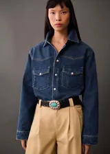 Camisa de jean azul con bolsillos de solapa en el pecho, manga larga con puños abotonados, diseño recto y oversize, cuello camisero y cierre delantero con botones.