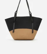 Bolso de playa grande de paja bicolor, negro en la parte superior y beige en la inferior, con asas de cuero sintético negro.