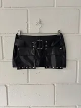 Minifalda negra de cuero sintético con cinturón con hebilla metálica, bolsillos delanteros con solapa y detalle de tachas.