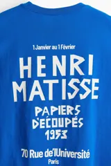 Remera azul con estampado frontal con texto en blanco 'HENRI MATISSE PAPIERS DECOUPÉS', corte amplio, cuello redondo y mangas cortas.