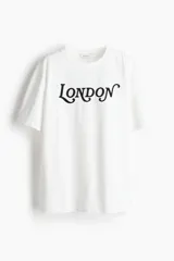 Remera blanca de algodón con cuello redondo y mangas cortas. Estampado frontal con la palabra "London" en letras negras con diseño ornamentado.
