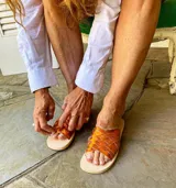 Sandalias chatas con tiras trenzadas de cuero color naranja metálico.