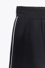 Falda midi negra de tiro alto con cintura elástica ajustable con cordones y detalle de vivo lateral blanco a contraste.