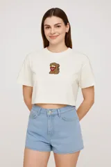 Remera cropped color crudo con estampado de oso de peluche con pañuelo rojo.
