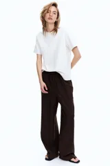 Pantalón marrón de corte holgado en tejido liviano de mezcla de lino. Modelo de tiro alto con cintura elástica y cordón para ajustar fino, bolsillos laterales discretos y piernas rectas.