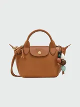 Bolso Longchamp modelo Le Pliage Ceramique XS, de cuero color caramelo, con doble asa corta y correa larga ajustable. Incluye charm colgante de cuentas de madera y cierre con broche a presión.