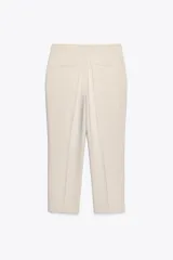 Pantalón negro tobillero de tiro alto con bolsillos delanteros y traseros. Tiene abertura lateral en el bajo y cierre frontal con cremallera y botón.