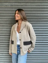 Campera de punto color beige con cuello tipo chal y cierre con tres botones. Tiene dos bolsillos frontales con solapa de cuero marrón.