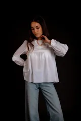 Camisa color crema con cuello alto y mangas largas con volados en los puños. Presenta detalles de crochet y broderie en el frente.