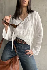 Blusa blanca de manga larga con detalles de encaje en el frente, mangas y cuello.