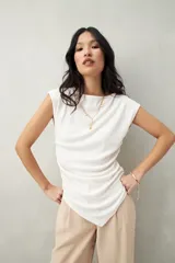 Top color beige de tejido acanalado, con cuello recto, sin mangas y terminación asimétrica en pico.