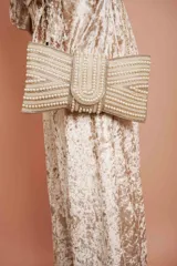 Clutch dorado con forma de moño, cubierto de perlas de diferentes tamaños y cadena dorada.