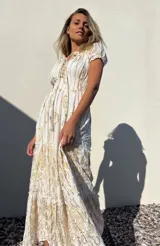 Vestido largo blanco con estampado dorado, escote en V con cordones y mangas cortas abullonadas.