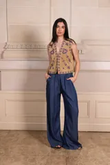 Chaleco color beige con bordados florales en tonos violeta y rosa, sin mangas y con cierre frontal con ganchos.