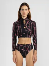 Crop top de bikini negro con estampado de cadenas rosas, cierre frontal con cremallera y detalle de flor en el cuello.