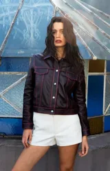 Campera corta de cuero ovino color borgoña, estilo jeanera, con cuello clásico, bolsillos con solapa y cierre frontal con broches metálicos.